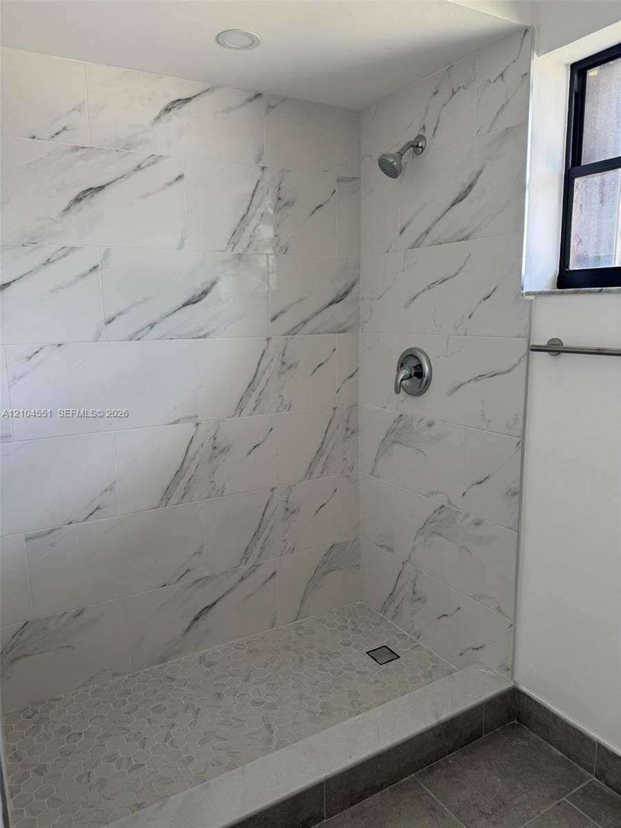 Walk-in shower featuring large-format stone-patterned tile walls, a pebble-finish floor, a recessed ceiling light, and a polished chrome fixture set