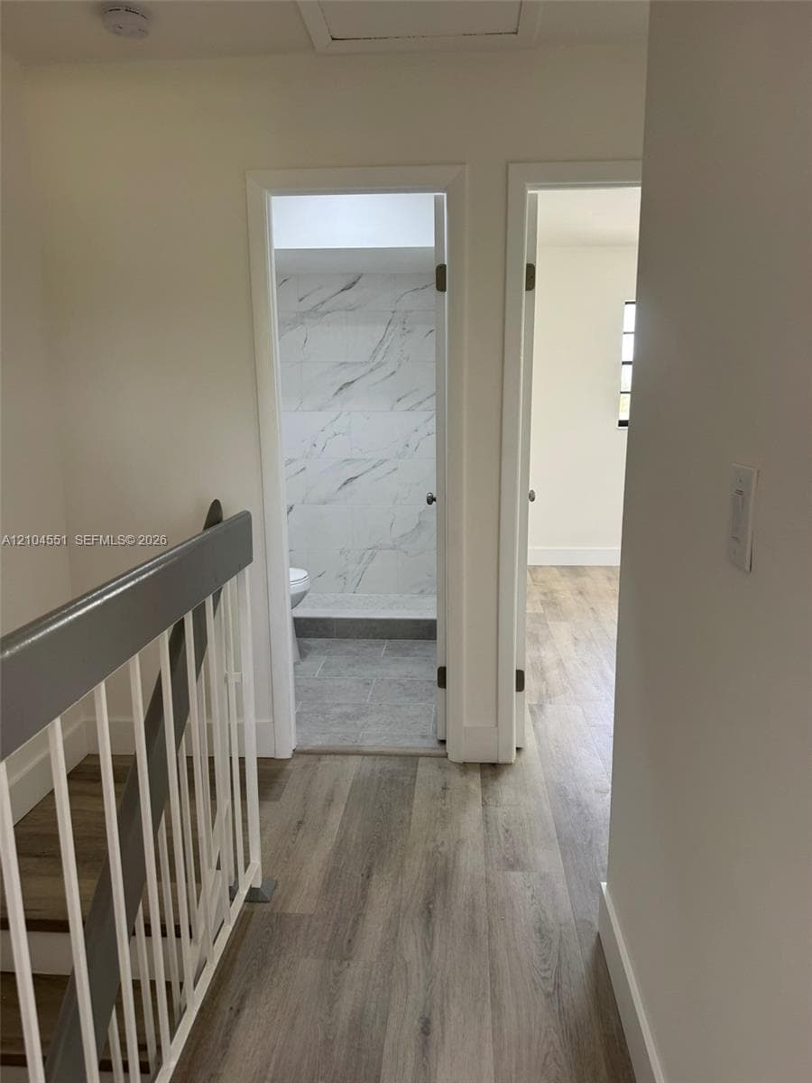 Staircase featuring a painted wood railing and balusters, wood-finish flooring, and a bathroom showcasing stone-finish wall tile