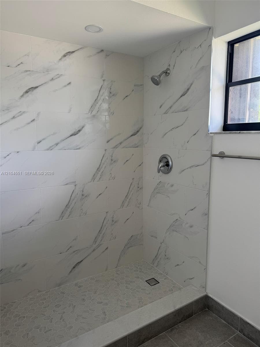 Walk-in shower featuring large-format stone-patterned wall tile, pebble-textured flooring, recessed lighting, and a metal-finish fixture