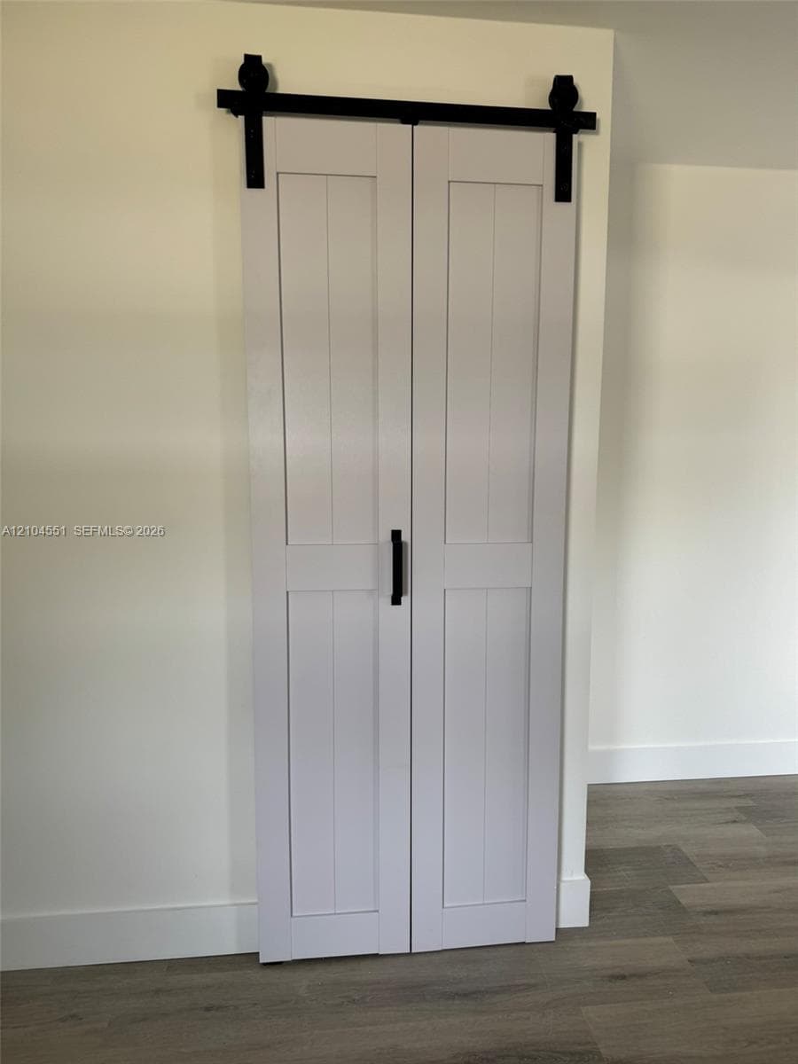 Double-panel sliding barn door featuring a matte black track system, vertical paneled construction, and matching matte black hardware