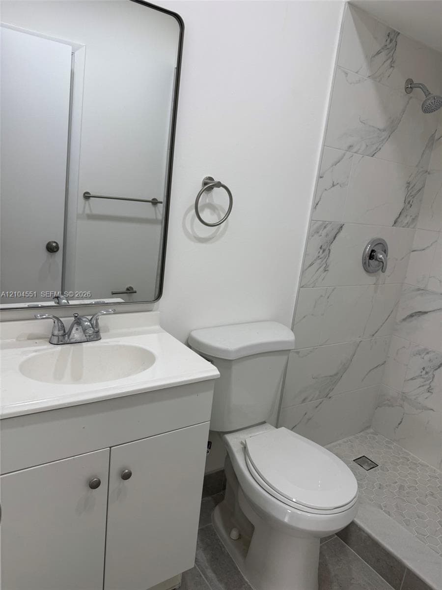 Bathroom featuring a vanity with an integrated sink, rectangular mirror with a dark frame, chrome fixtures, and a shower stall with stone-patterned tile surround