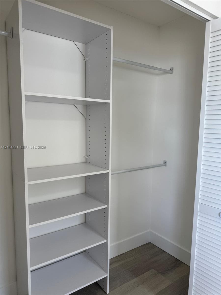 Reach-in closet featuring built-in vertical shelving, dual metal hanging rods, and wood-finish flooring