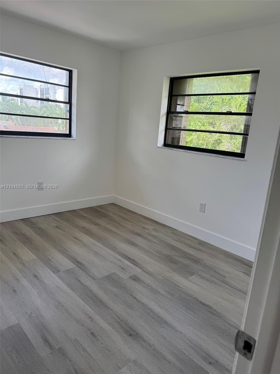 Room featuring wood-finish flooring, neutral walls, and dual louvered windows with black frames
