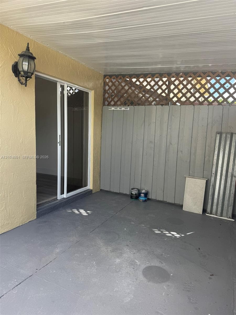 Covered patio featuring concrete flooring, sliding glass door access, exterior wall-mounted lighting, and a vertical wood privacy screen with lattice detailing