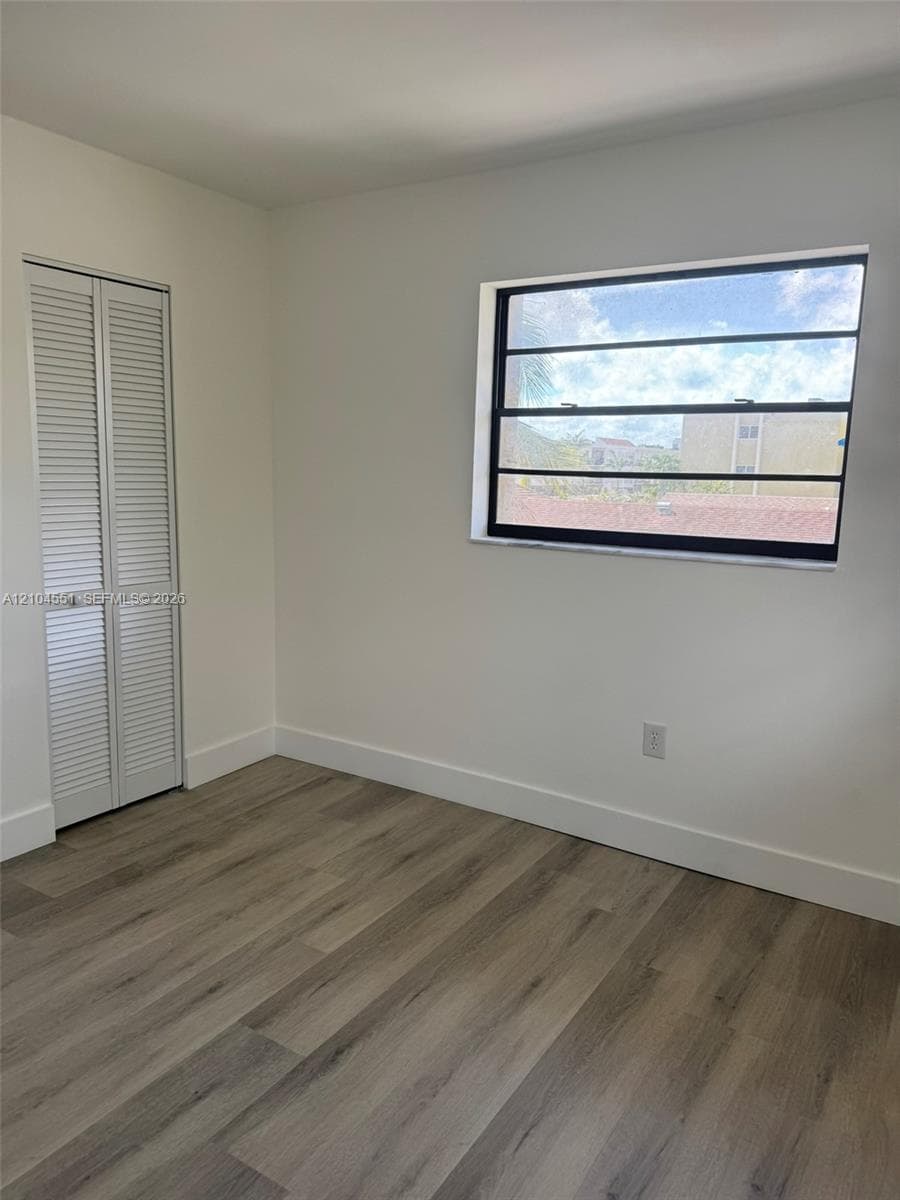 Wood-finish flooring, white louvered closet doors, and a horizontal jalousie window