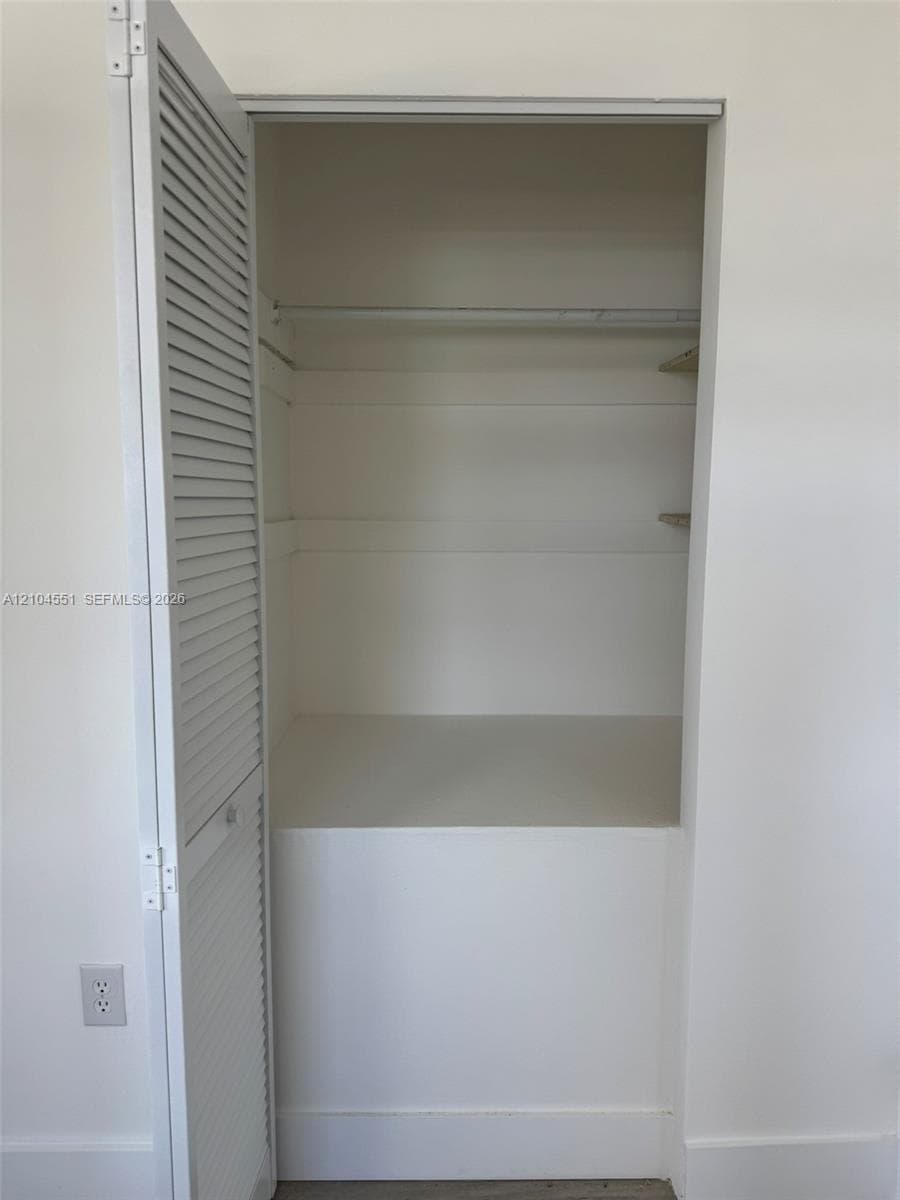 Storage closet featuring louvered bi-fold doors, built-in shelving, and a garment rod