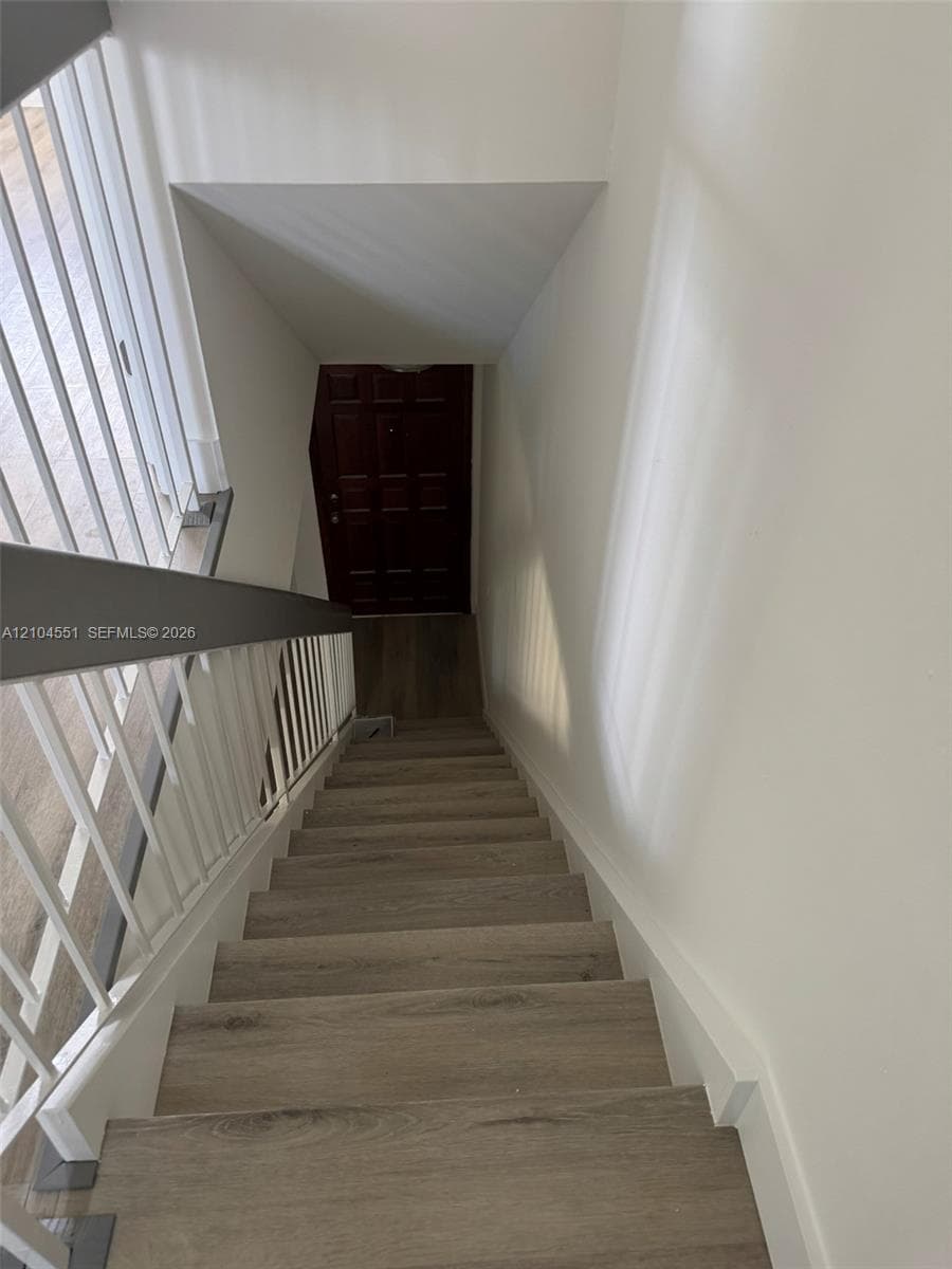 Staircase featuring wood-finish treads, a white metal spindle railing, and a dark-finish solid panel door