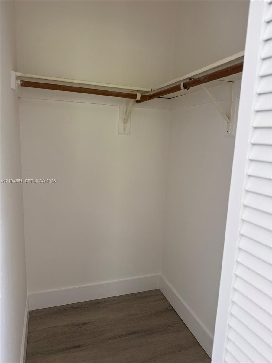 Storage area featuring wood-finish flooring, white louvered doors, and built-in shelving with a hanging rod