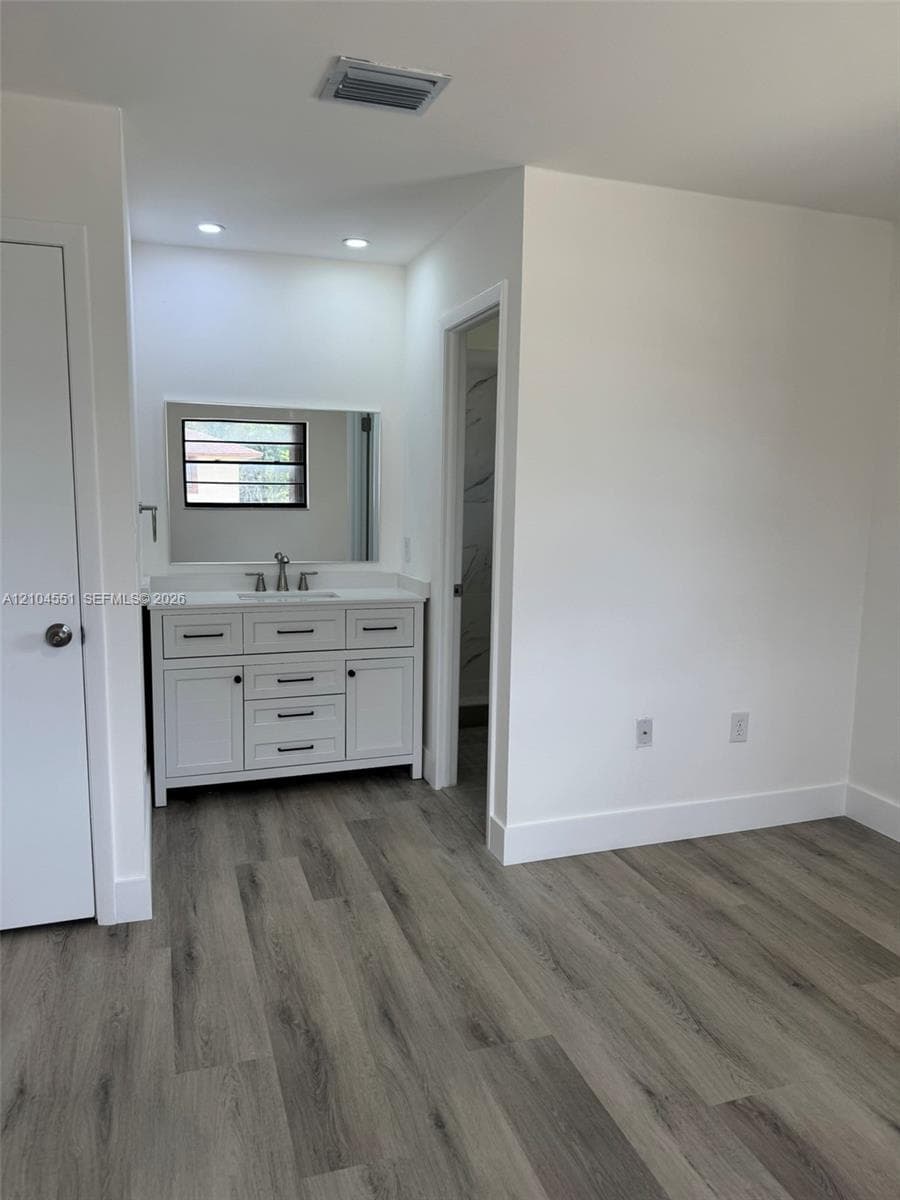 White vanity with matte black hardware, integrated countertop, recessed lighting, and wood-finish flooring