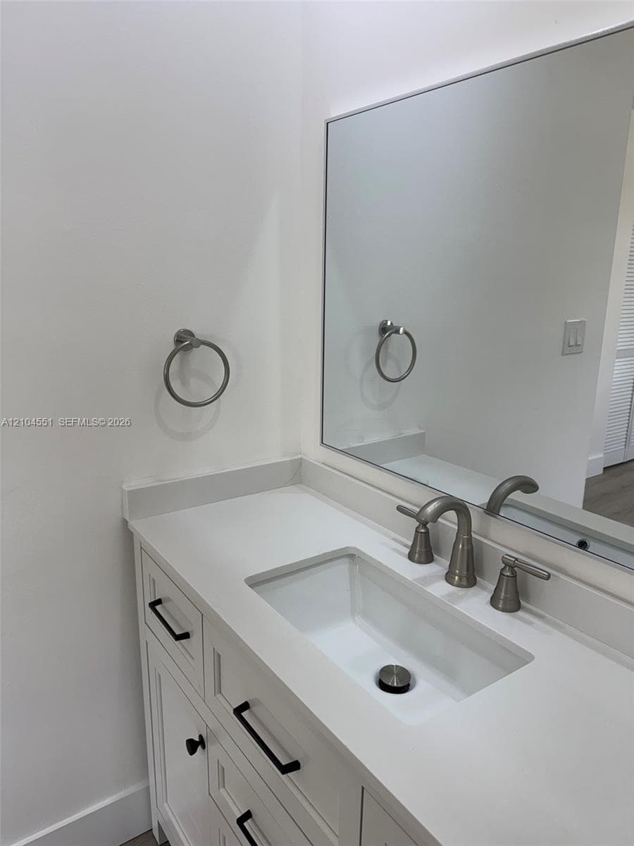 White vanity featuring an undermount rectangular sink, light-toned solid surface countertop, brushed nickel widespread faucet, and matte black hardware paired with a wall-mounted mirror