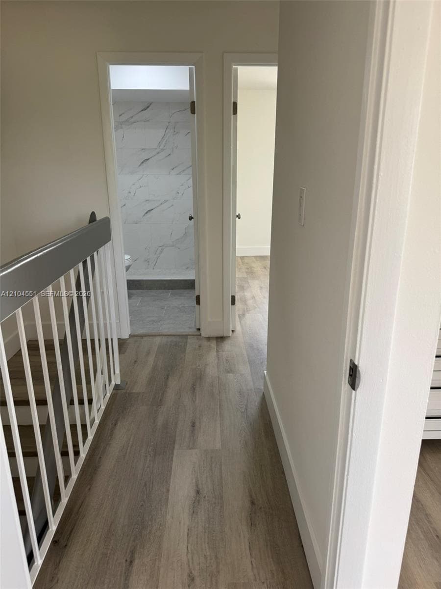 Hallway featuring wood-finish flooring, a painted metal railing, and doorways revealing stone-patterned tile wall accents