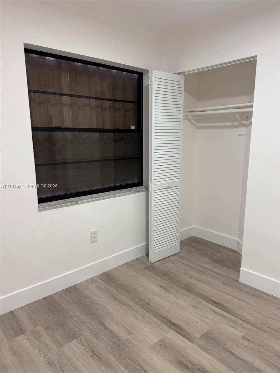 Room featuring wood-finish flooring, a window with a black frame and stone-look sill, and a closet with white louvered doors