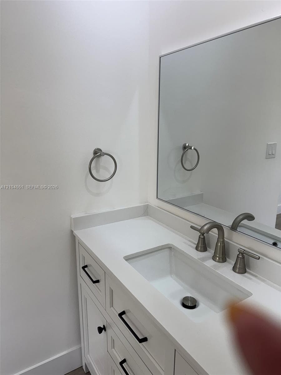 White vanity featuring a solid surface countertop, integrated rectangular sink, brushed nickel widespread faucet, matte black hardware, and a frameless wall-mounted mirror