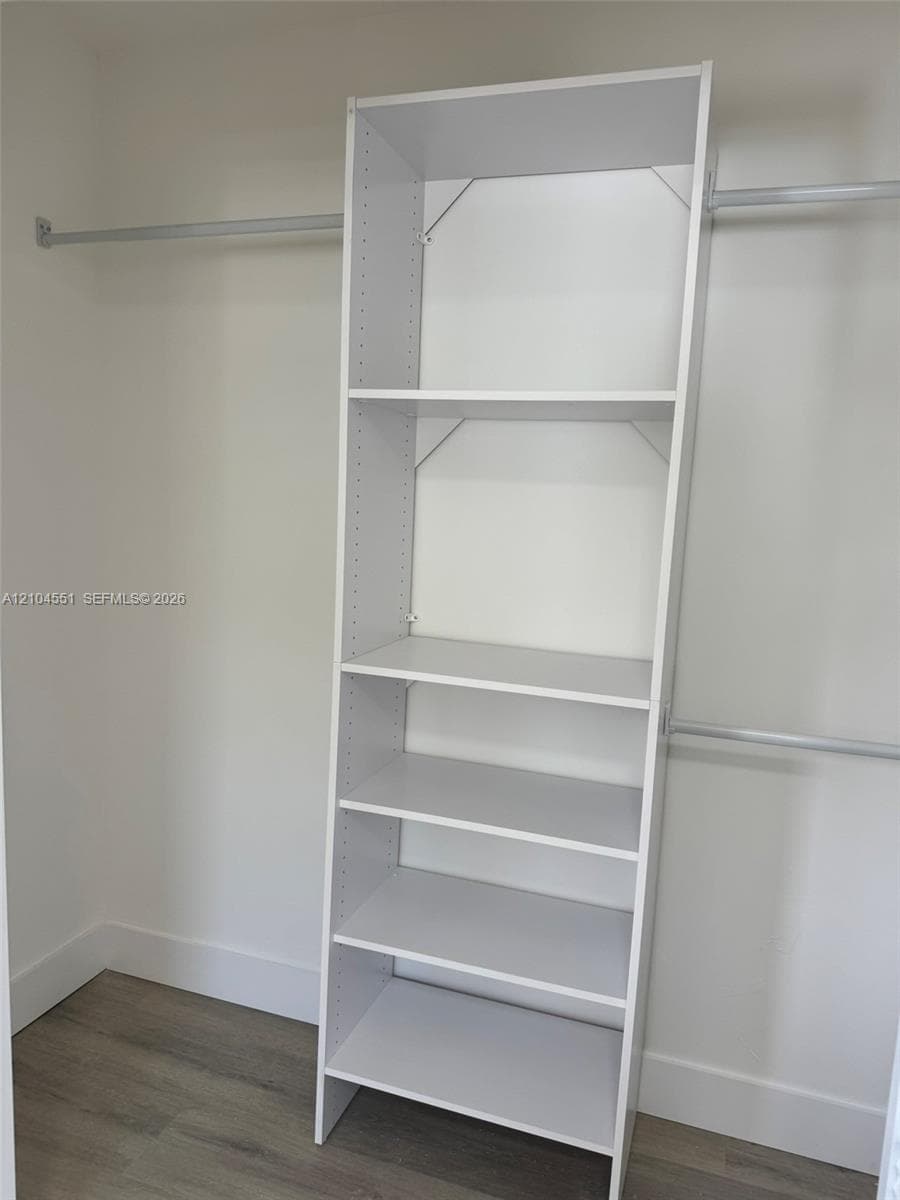 Custom walk-in closet featuring white built-in shelving, adjustable storage tiers, and dual metal hanging rods over wood-finish flooring