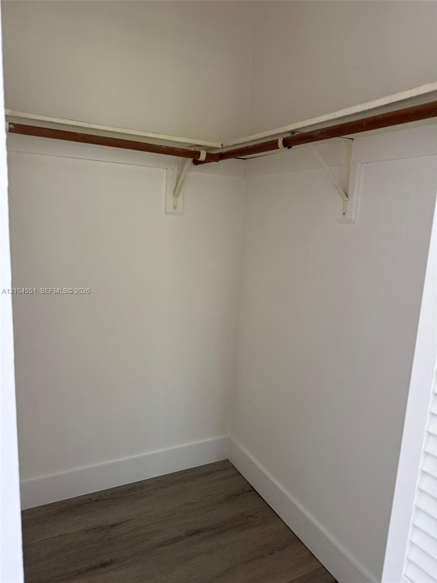 Storage area featuring wood-finish flooring, white walls, and built-in shelving with hanging rods