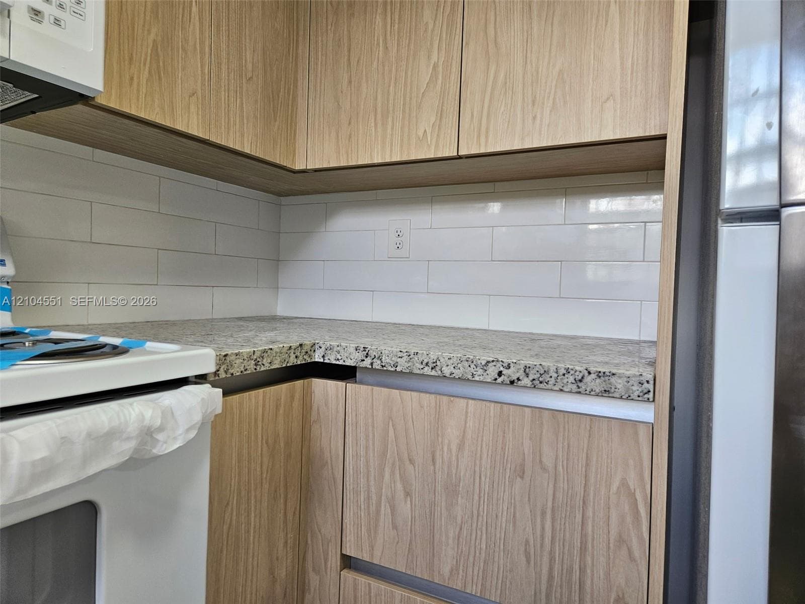 Flat-panel wood-finish cabinetry, stone-finish countertops, and a white subway tile backsplash