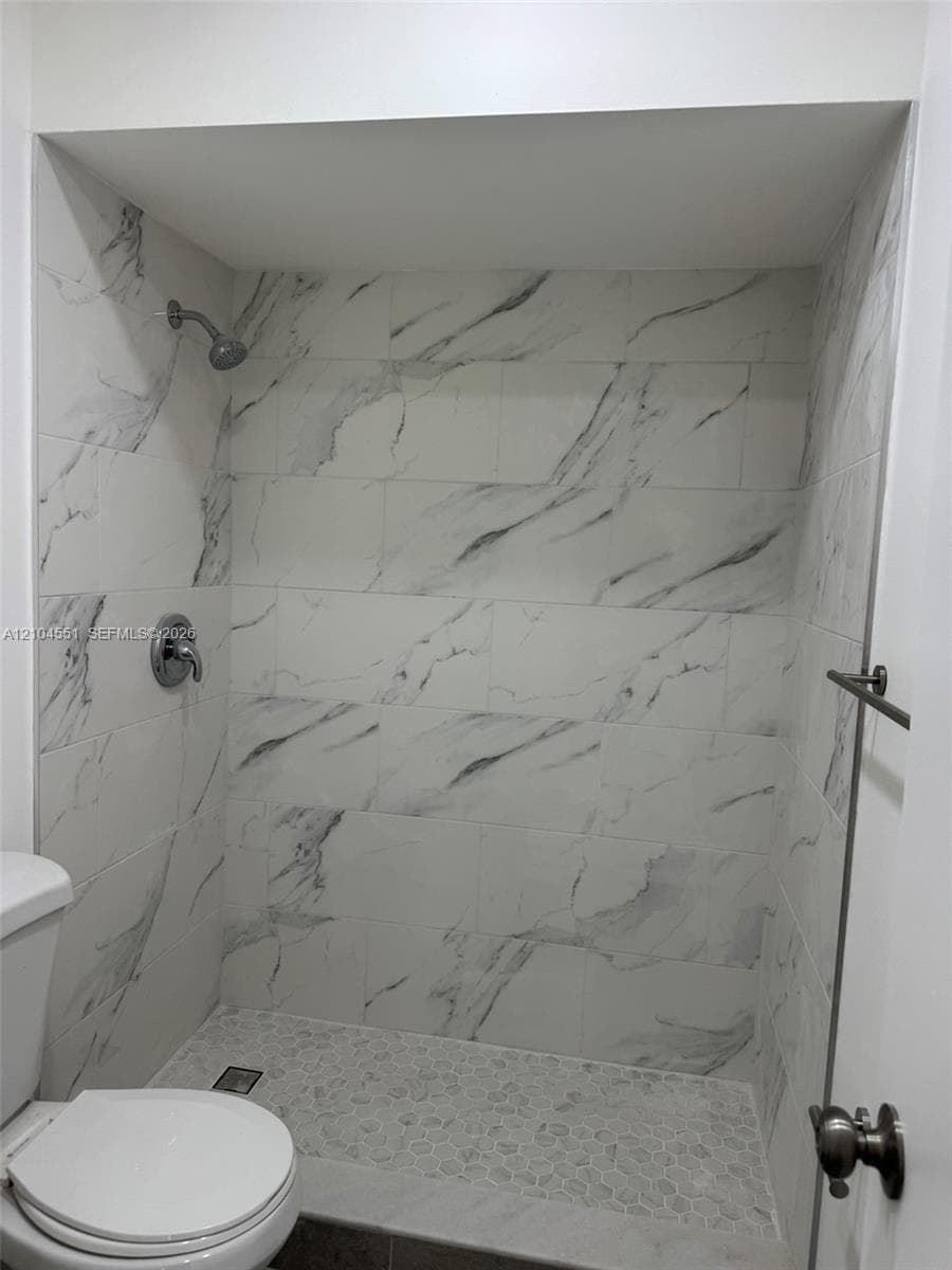 Walk-in shower featuring large-format stone-patterned wall tile, pebble-stone flooring, and chrome fixtures
