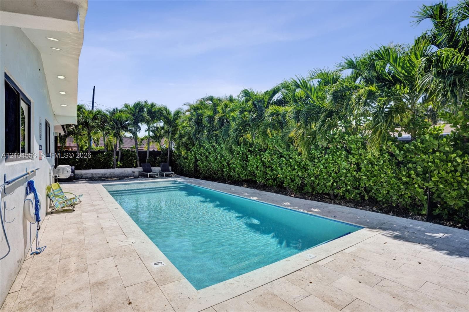 Rectangular swimming pool featuring stone-paver decking and mature perimeter hedge landscaping