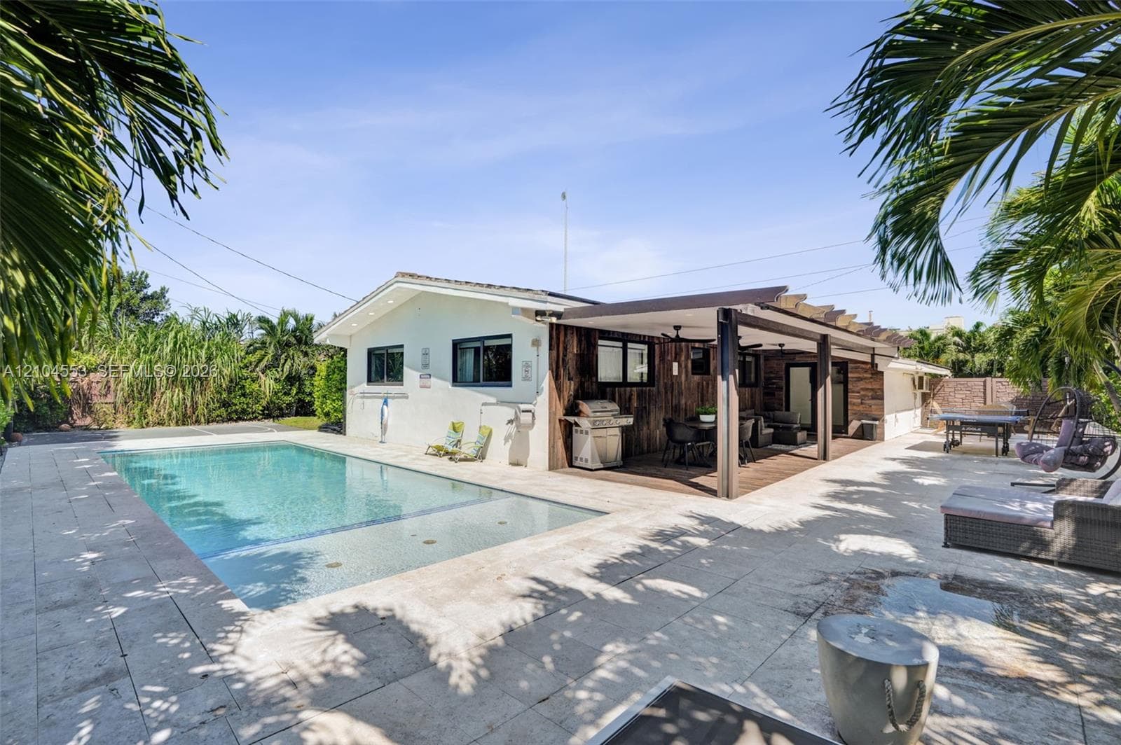In-ground swimming pool featuring a stone-paver deck, expansive wood-finished covered patio, and exterior wood paneling