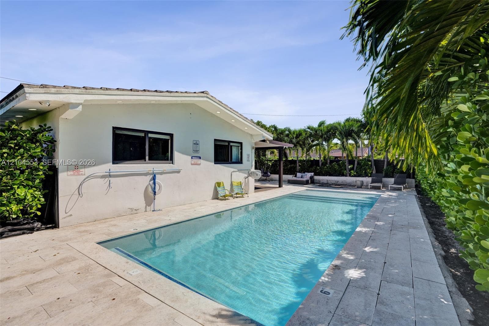 Rectangular in-ground swimming pool featuring stone-paver decking and mature privacy landscaping