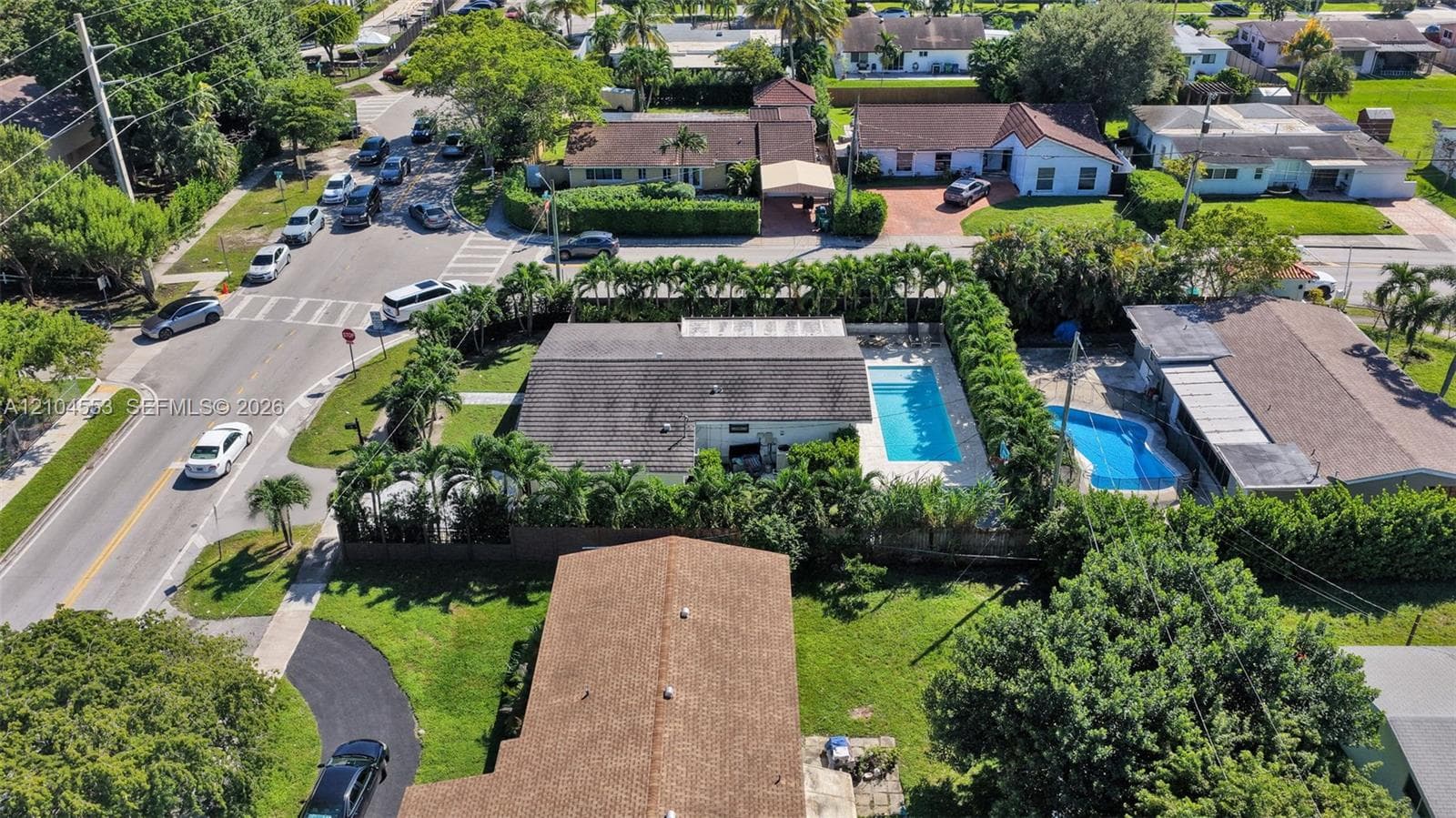 Aerial perspective featuring a rectangular swimming pool, concrete patio, perimeter hedges, and a multi-pitched shingle roof