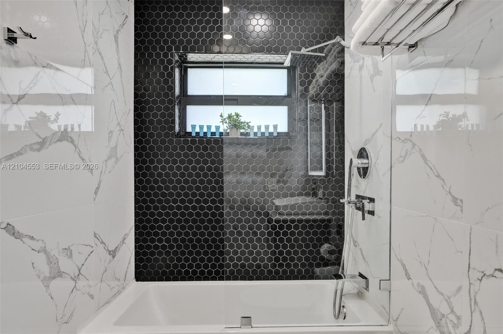 Walk-in shower featuring large-format veined tile walls, a matte black hexagonal mosaic tile accent wall, built-in window, glass partition, and wall-mounted shower hardware