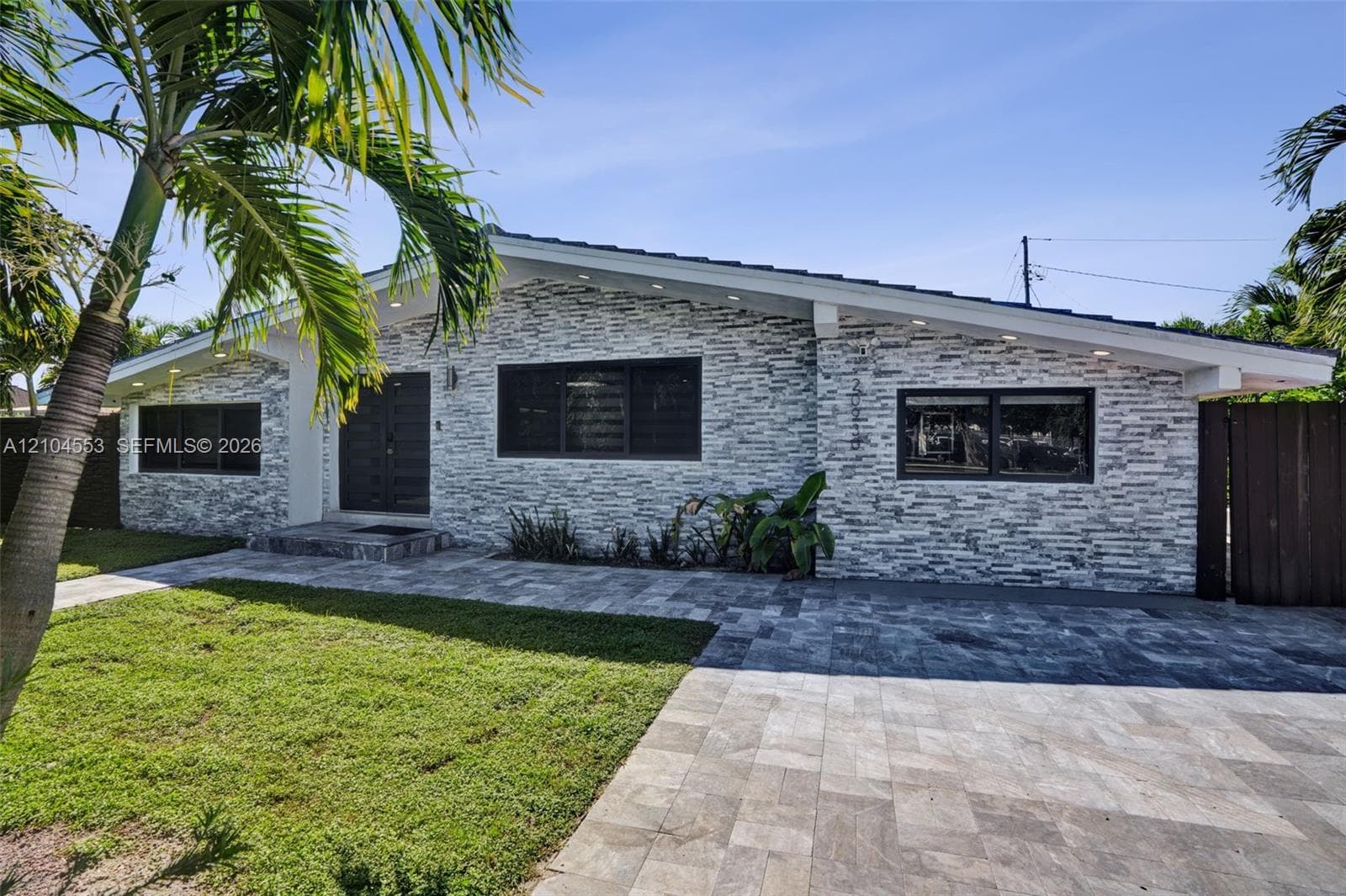 Mid-century modern exterior featuring natural stone veneer, a low-pitched roofline, stone-paver driveway, and manicured lawn