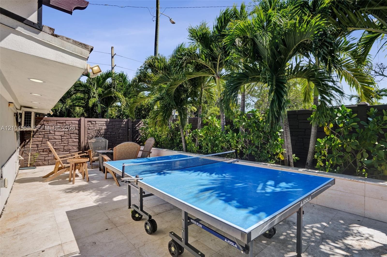 Paved outdoor patio featuring stone-tile flooring, perimeter masonry walls with stone veneer accents, and mature palm trees