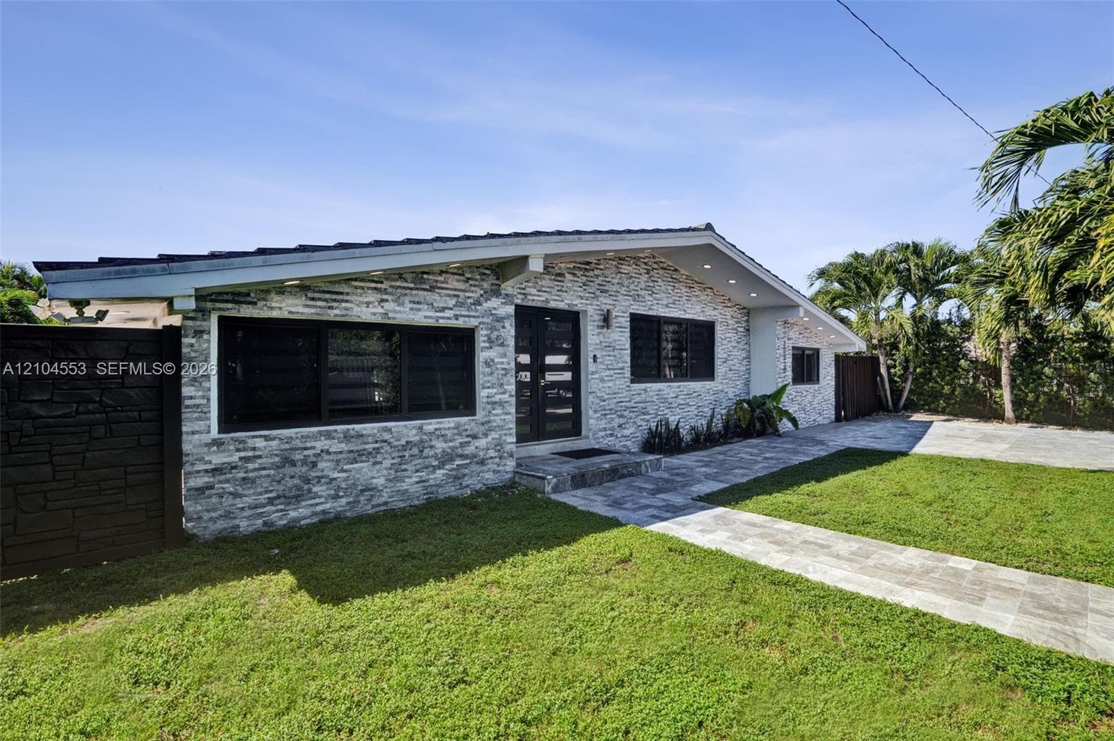 Single-story residence featuring a stacked stone exterior, low-pitch roofline, paver walkway, and dark-frame windows