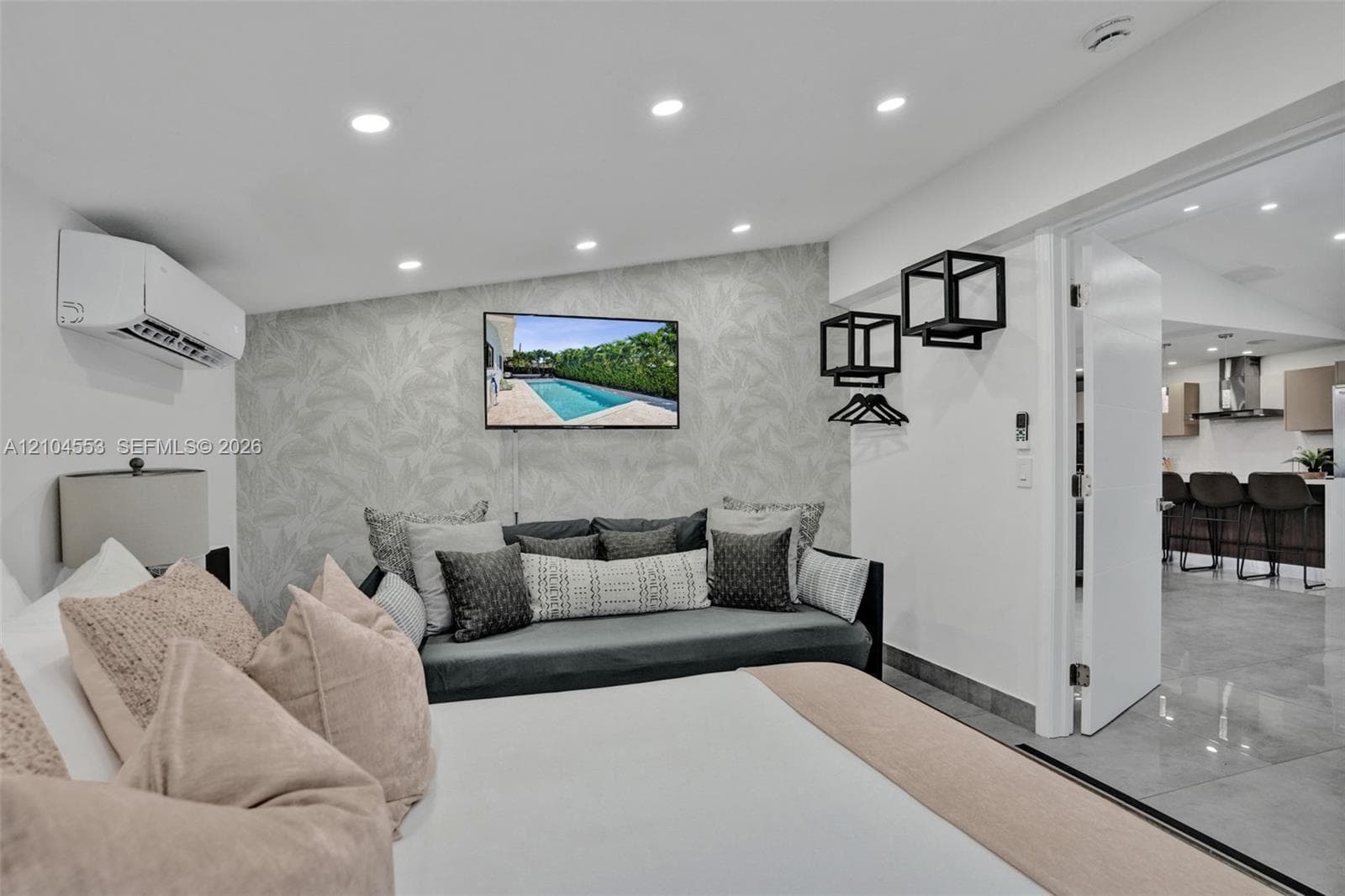 Neutral-toned wallpaper accent wall, wall-mounted mini-split HVAC unit, recessed lighting, and black geometric wall-mounted shelving