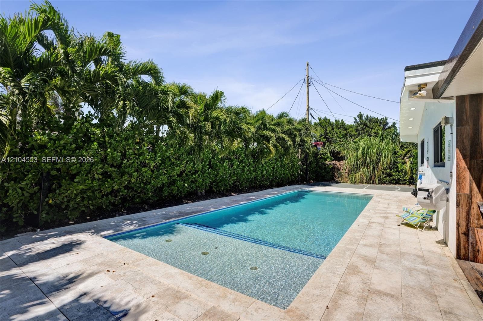 Rectangular swimming pool with a sun shelf, stone-paver decking, and mature privacy hedging