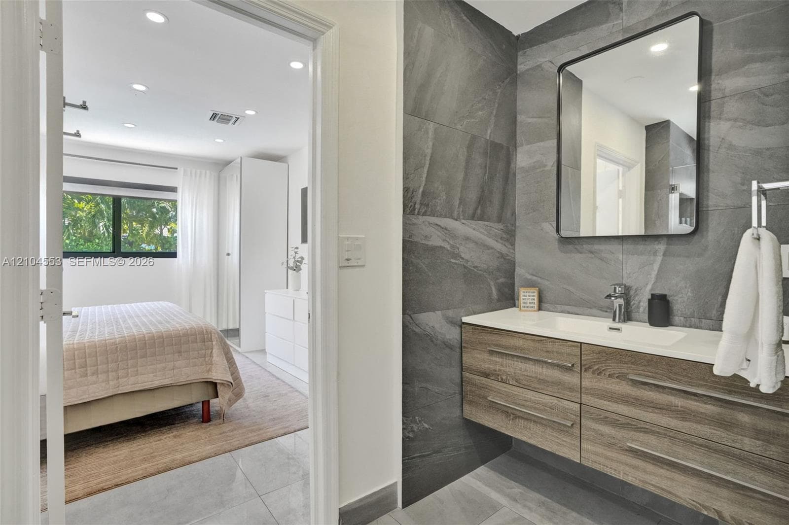 Floating vanity with wood-finish cabinetry, rectangular integrated sink, wall-mounted faucet, and large-format gray stone-finish wall tile