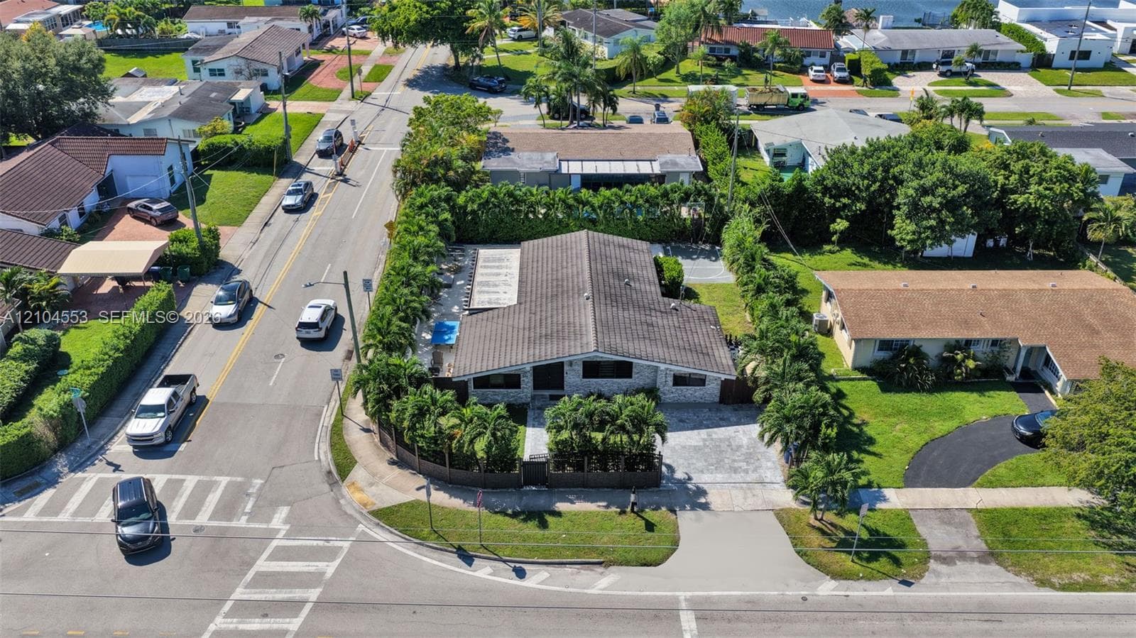 Aerial view of a residential property featuring a tiled roof, paver driveway, swimming pool, and mature perimeter hedging