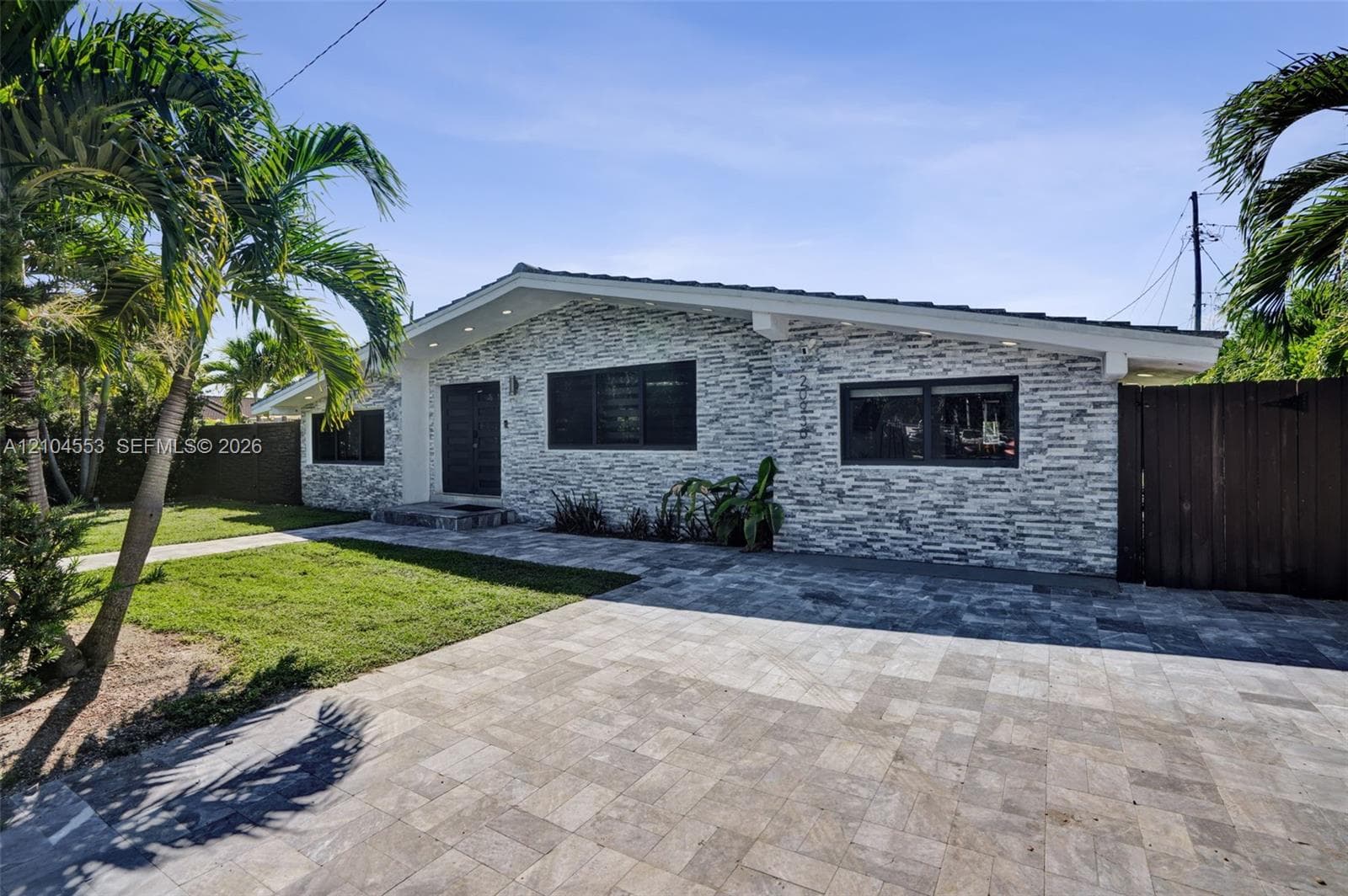 Single-story exterior featuring stacked stone cladding, paved driveway, low-pitch roofline, and recessed exterior lighting