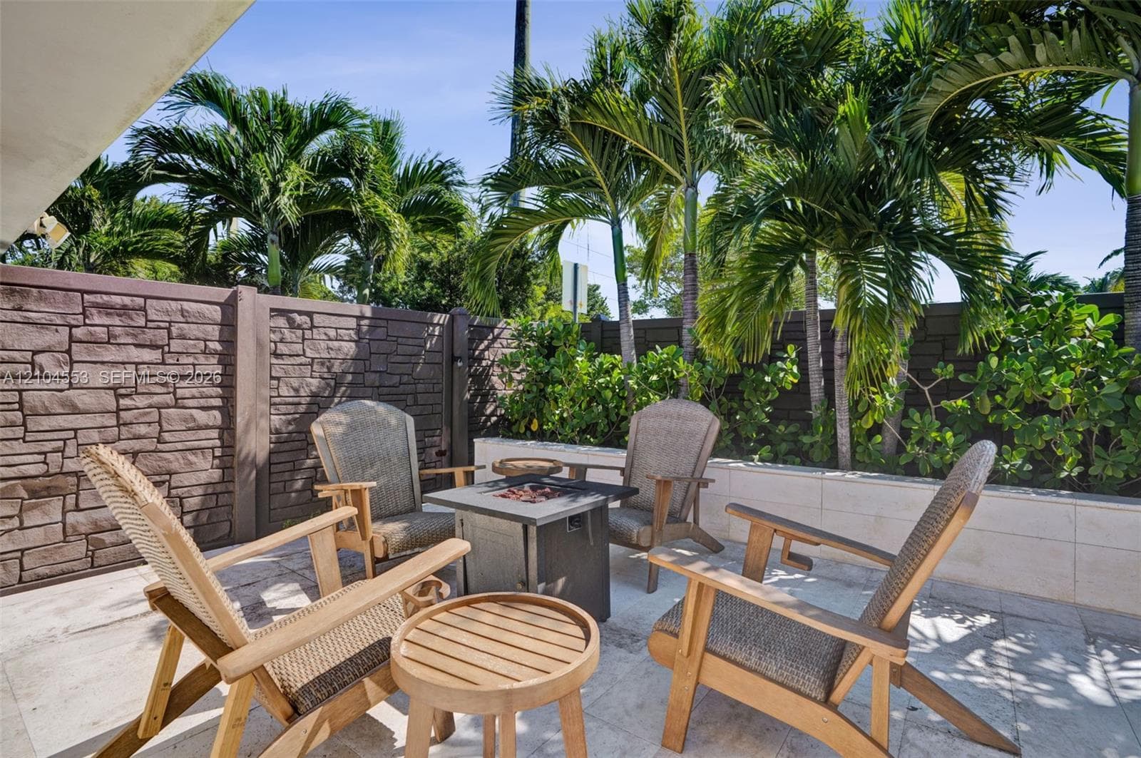 Outdoor patio featuring natural stone tile flooring, decorative stone-veneer privacy wall, smooth-finish stone retaining wall, and mature palm trees