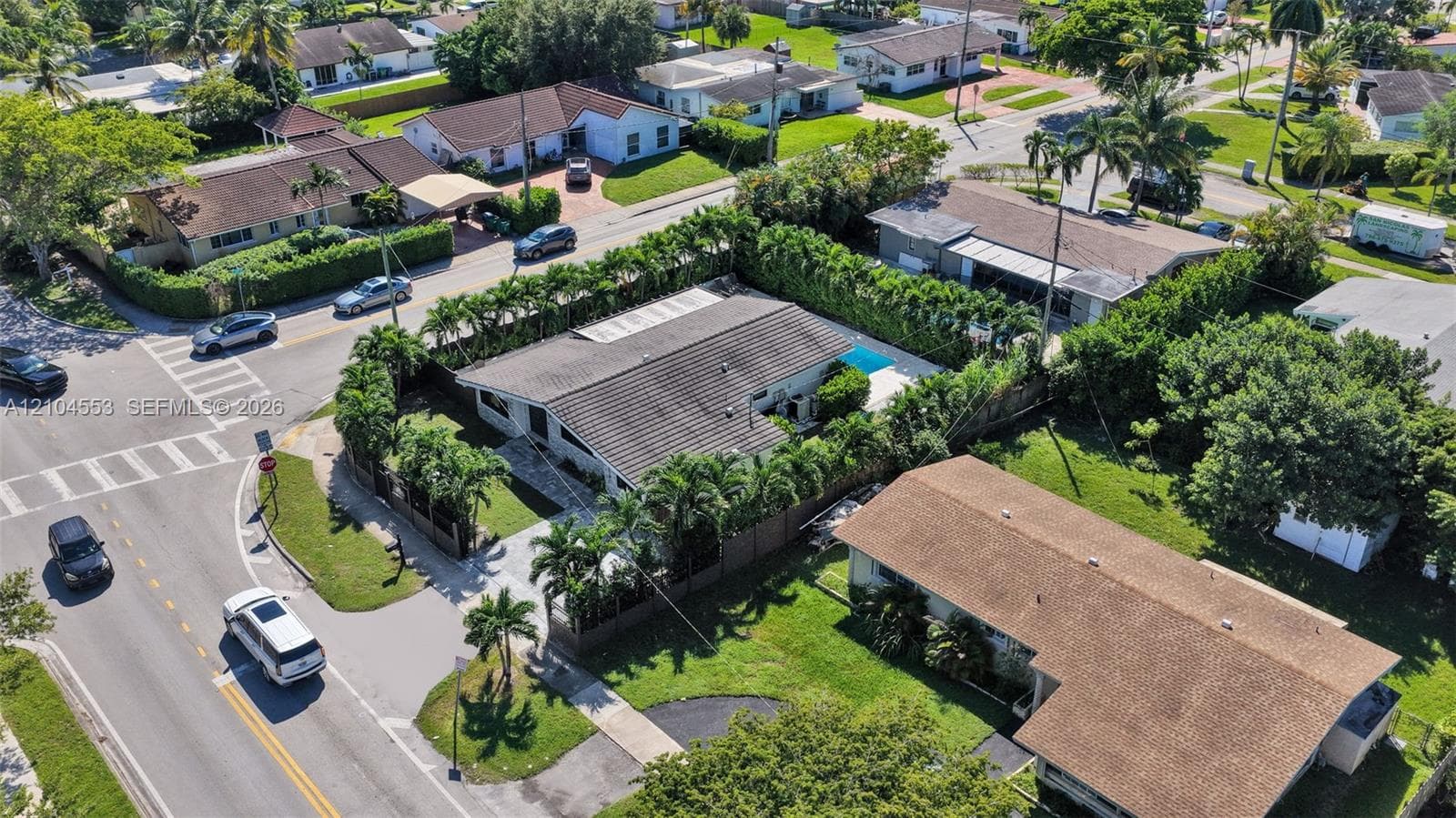 Corner lot residence featuring a tile roof, privacy hedge, and a rectangular in-ground swimming pool