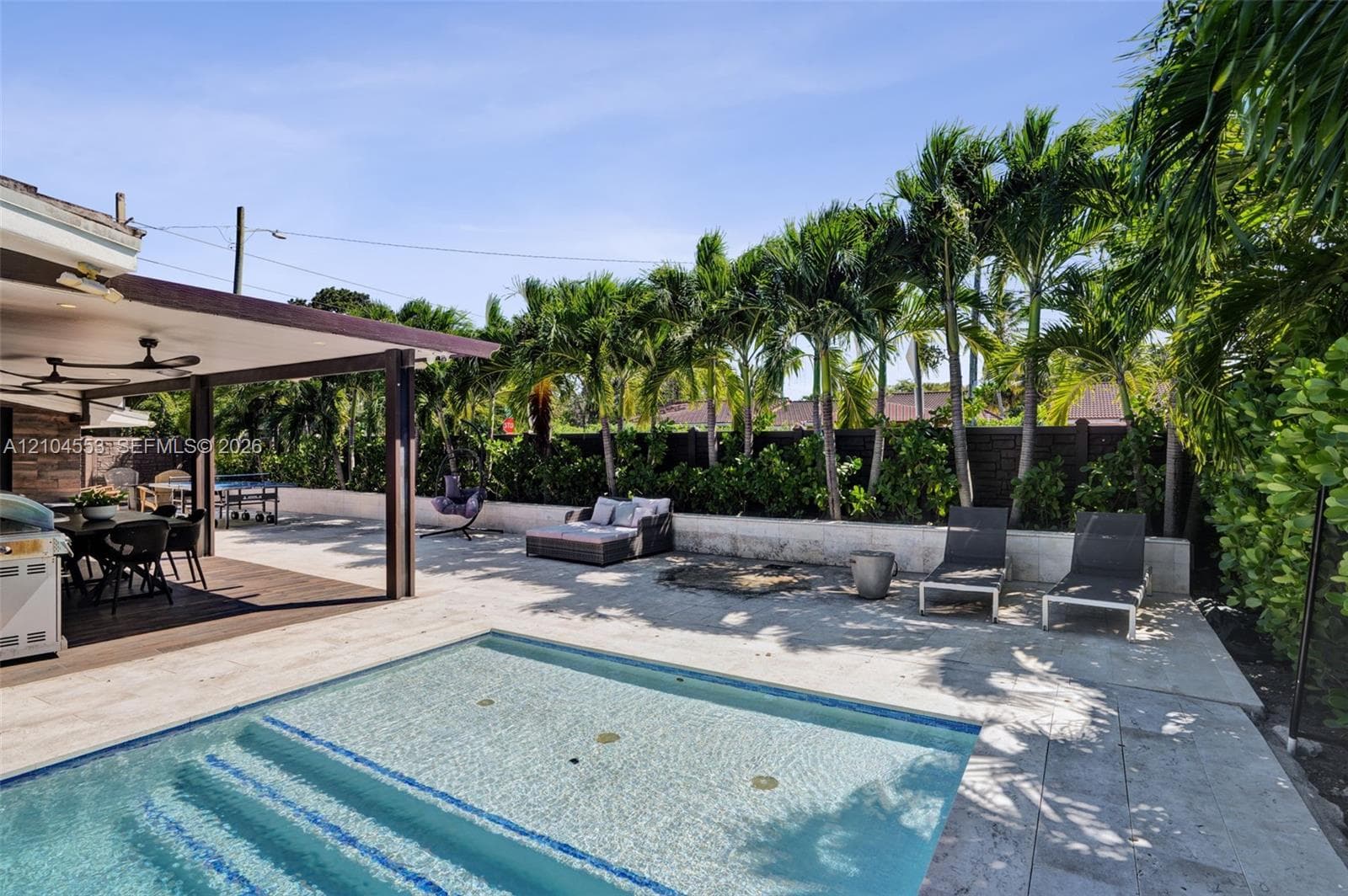 Backyard area featuring a covered patio, swimming pool with built-in stairs, stone pool decking, and mature perimeter palm trees