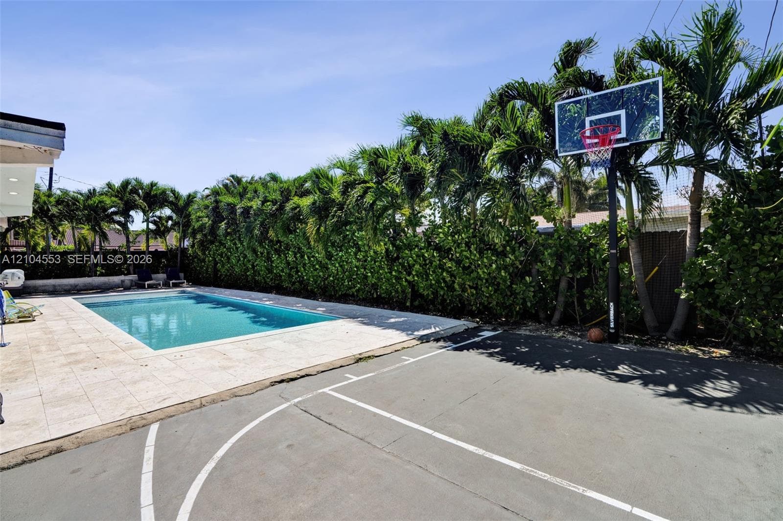 Outdoor recreation area featuring a paved basketball court, swimming pool with stone decking, and mature perimeter palm trees