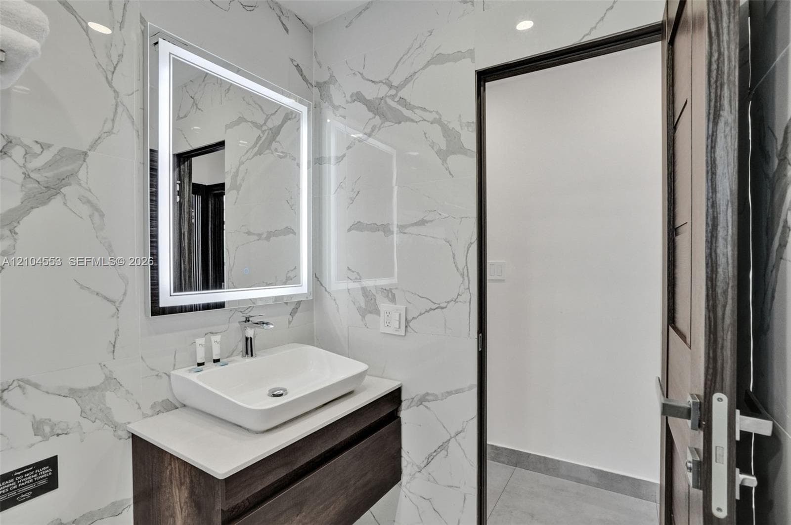 Floating vanity with a rectangular vessel sink and countertop, backlit rectangular mirror, and full-height stone-finish wall tile