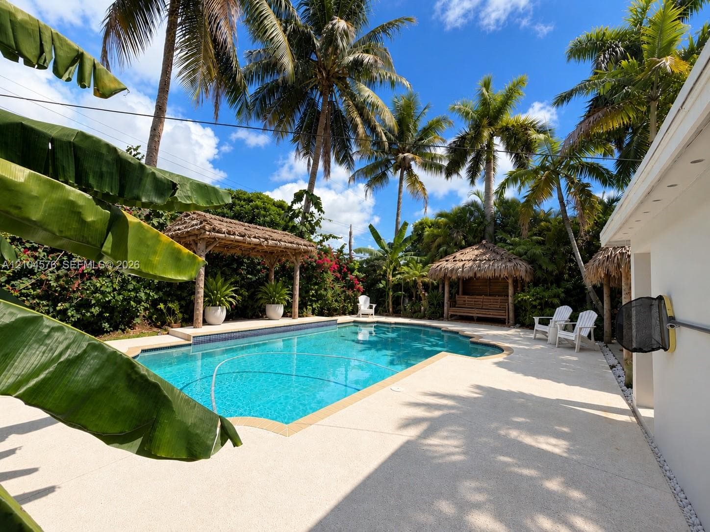 Swimming pool featuring a concrete deck, multiple thatched-roof cabanas, and mature palm trees