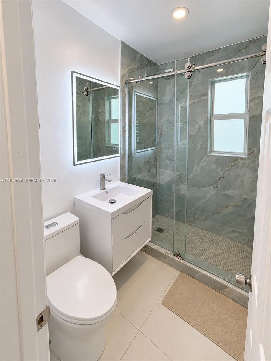 Floating vanity with a modern sink, LED-backlit mirror, glass-enclosed shower with floor-to-ceiling tile, and recessed lighting