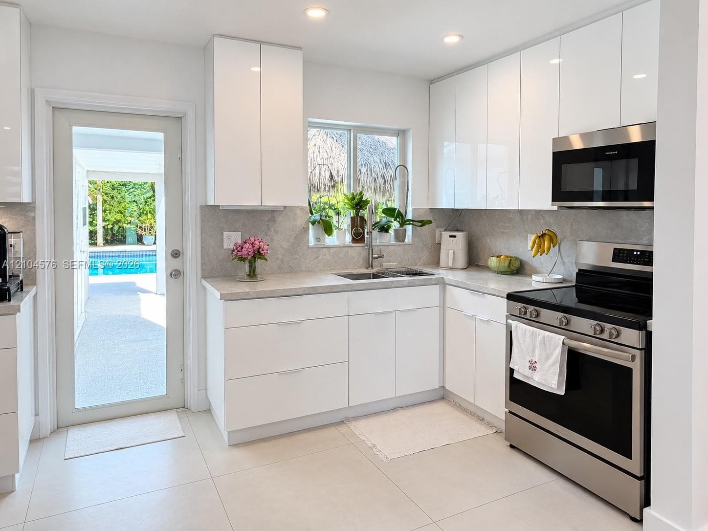 Kitchen featuring high-gloss white cabinetry, stone-finish countertops, stainless steel appliances, recessed ceiling lighting, and a glass-paneled exterior door