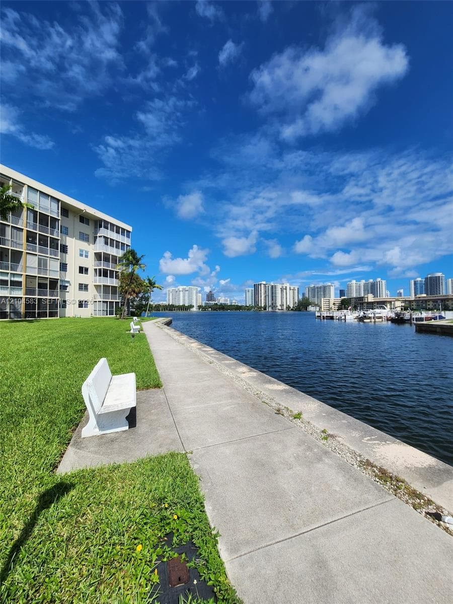 Waterfront property featuring a paved walking path, manicured lawn, and bulkheaded shoreline