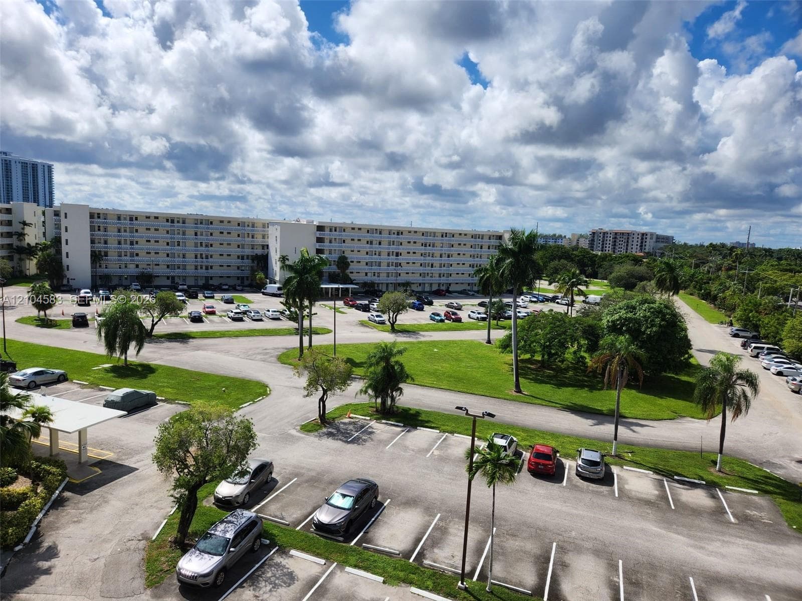 Multi-story apartment complex featuring surface parking lots, covered parking structures, mature palm trees, and expansive green space