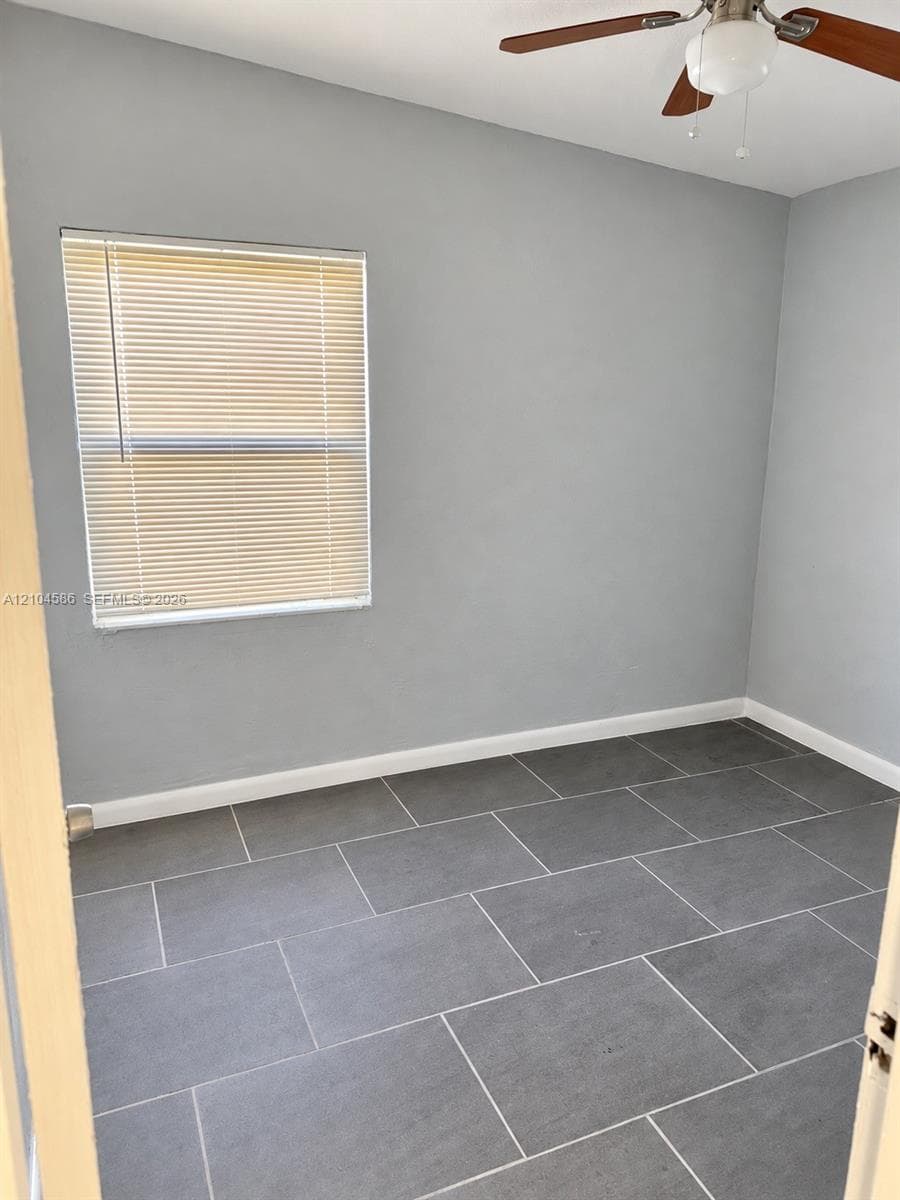 Neutral-toned interior room featuring large-format tile flooring, a window with horizontal blinds, and a ceiling fan with integrated light fixture