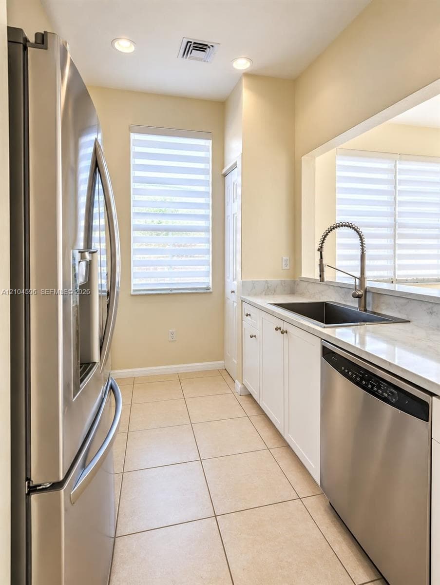 Kitchen featuring stainless steel appliances, white cabinetry, solid surface countertops, a deep-basin sink with a pull-down faucet, and ceramic tile flooring