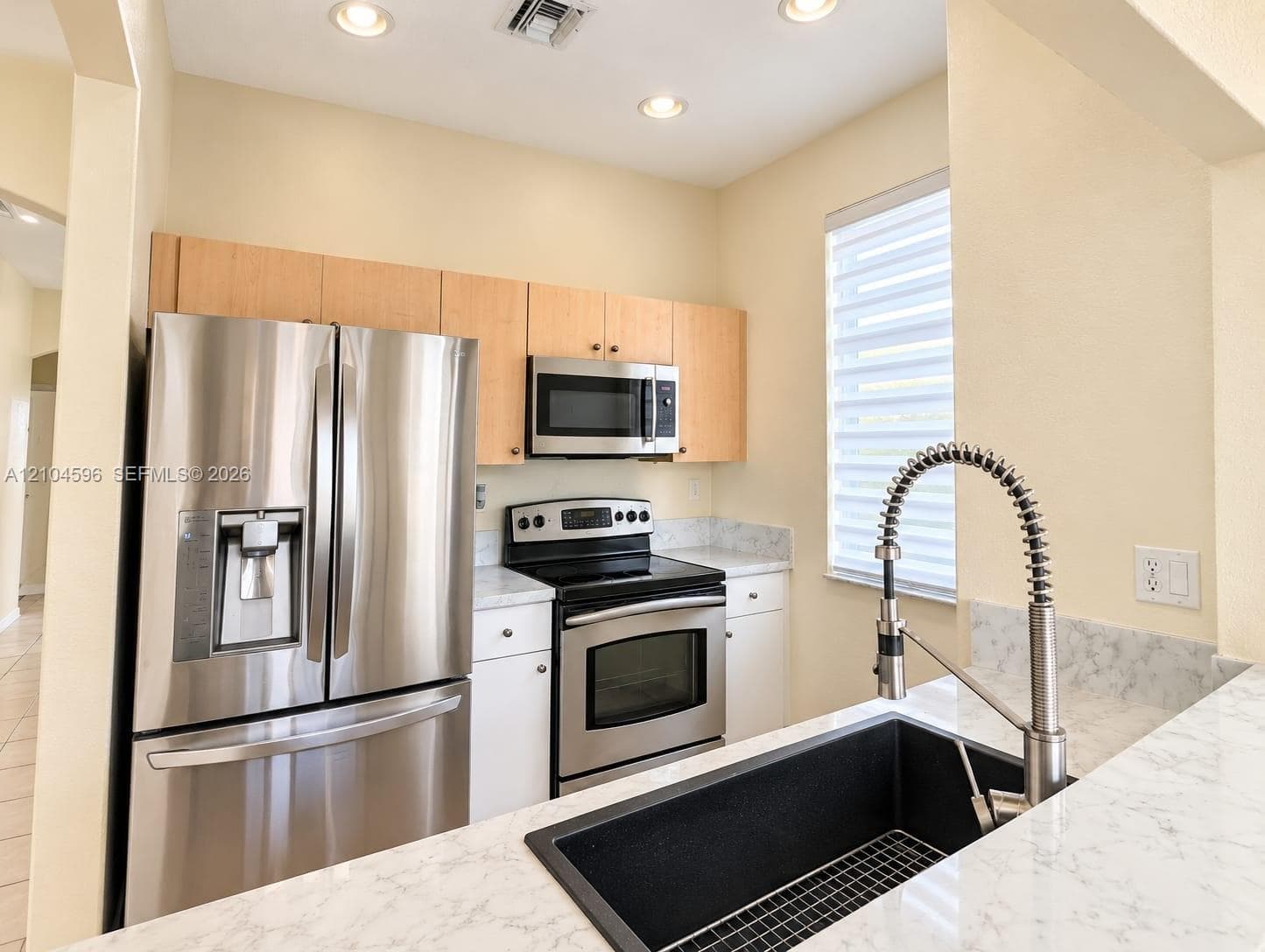 Kitchen featuring stainless steel appliances, light wood-finish cabinetry, stone-patterned countertops, a deep undermount sink with a gooseneck faucet, and recessed lighting