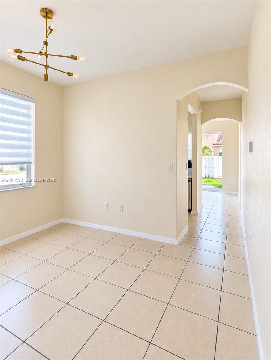 Interior space featuring large-format tile flooring, a modern multi-arm brass finish chandelier, neutral wall tones, and architectural arched doorways
