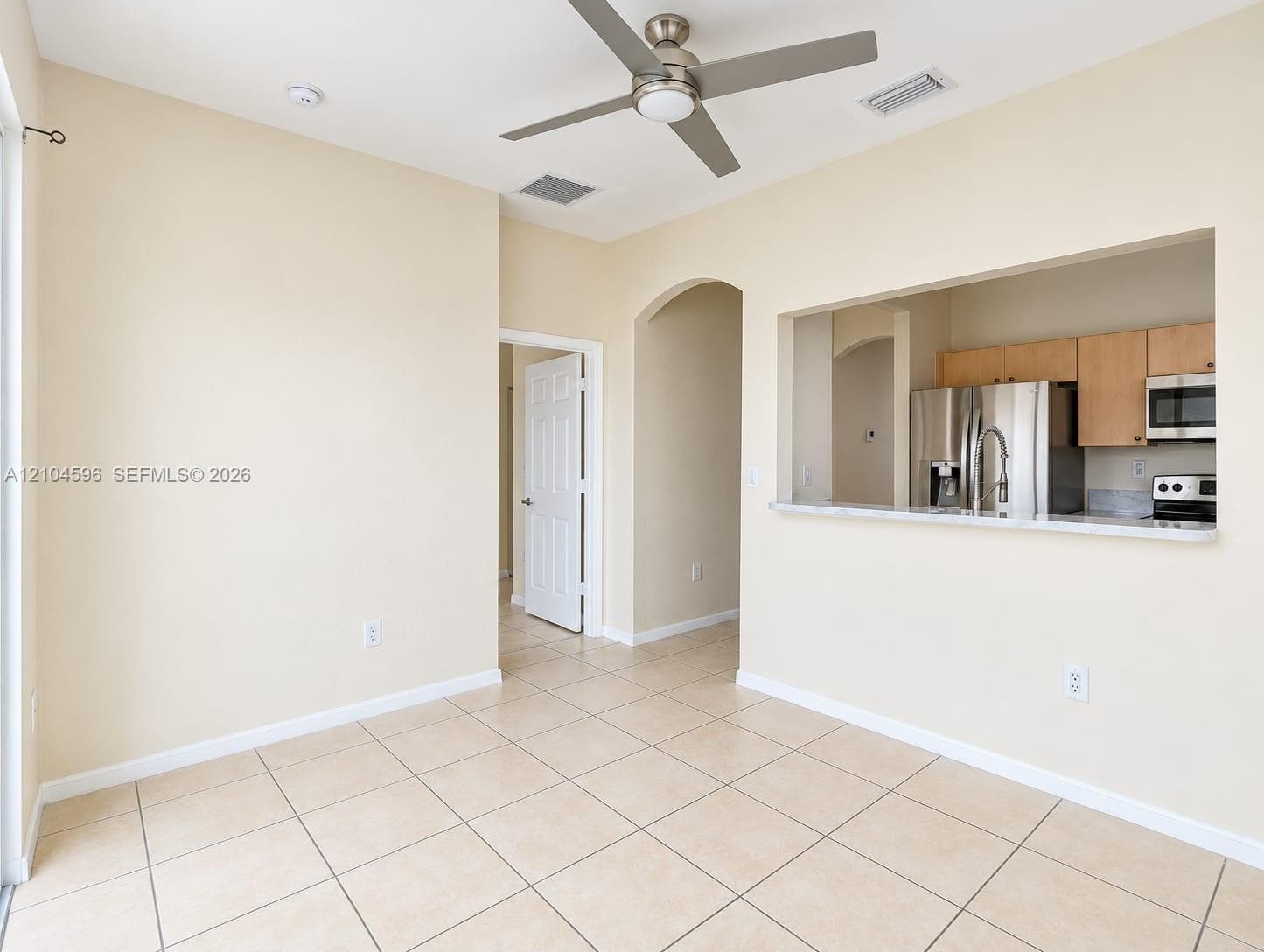 Tile flooring, ceiling fan with integrated lighting, pass-through opening to kitchen, stainless steel kitchen appliances, and shaker-style cabinetry