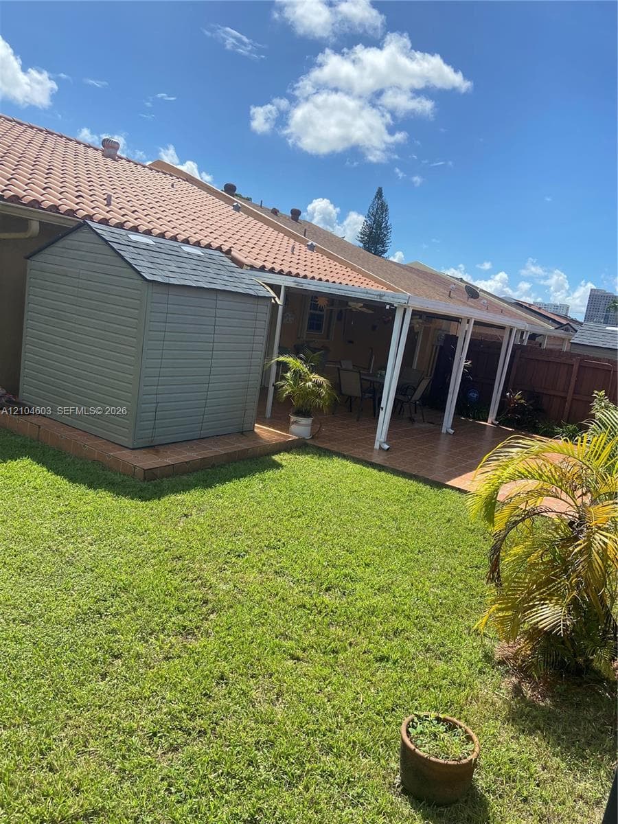 Expansive backyard featuring a manicured lawn, an outdoor shed on a raised platform, and a covered patio with a tile roof